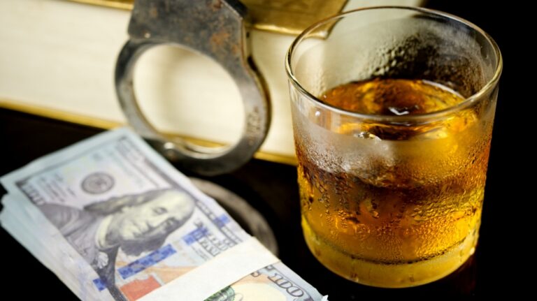 money next to glass of whiskey and handcuffs